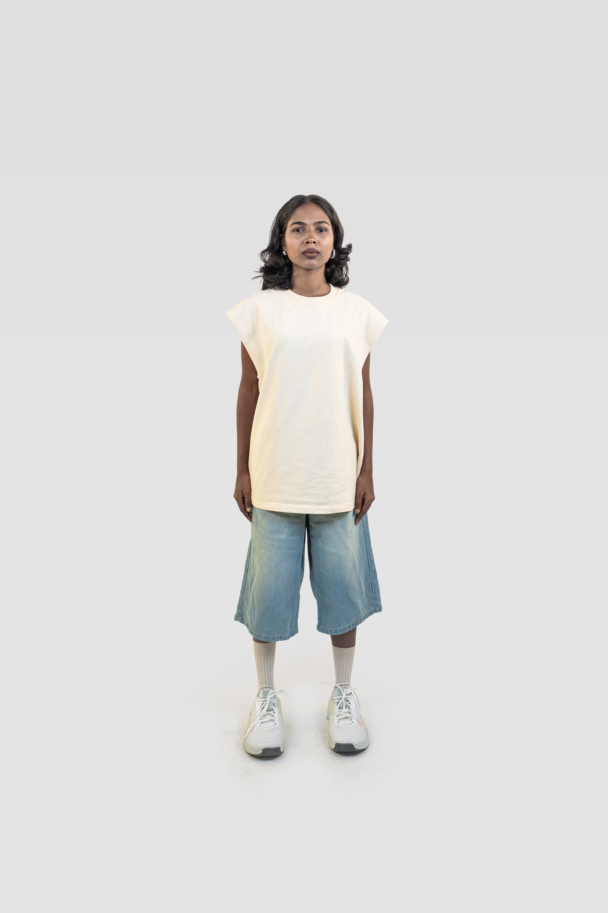 Full-body front view of model wearing the Harper Slein Foundation Tank in OG Off White, paired with blue shorts and sneakers, on a light gray background.