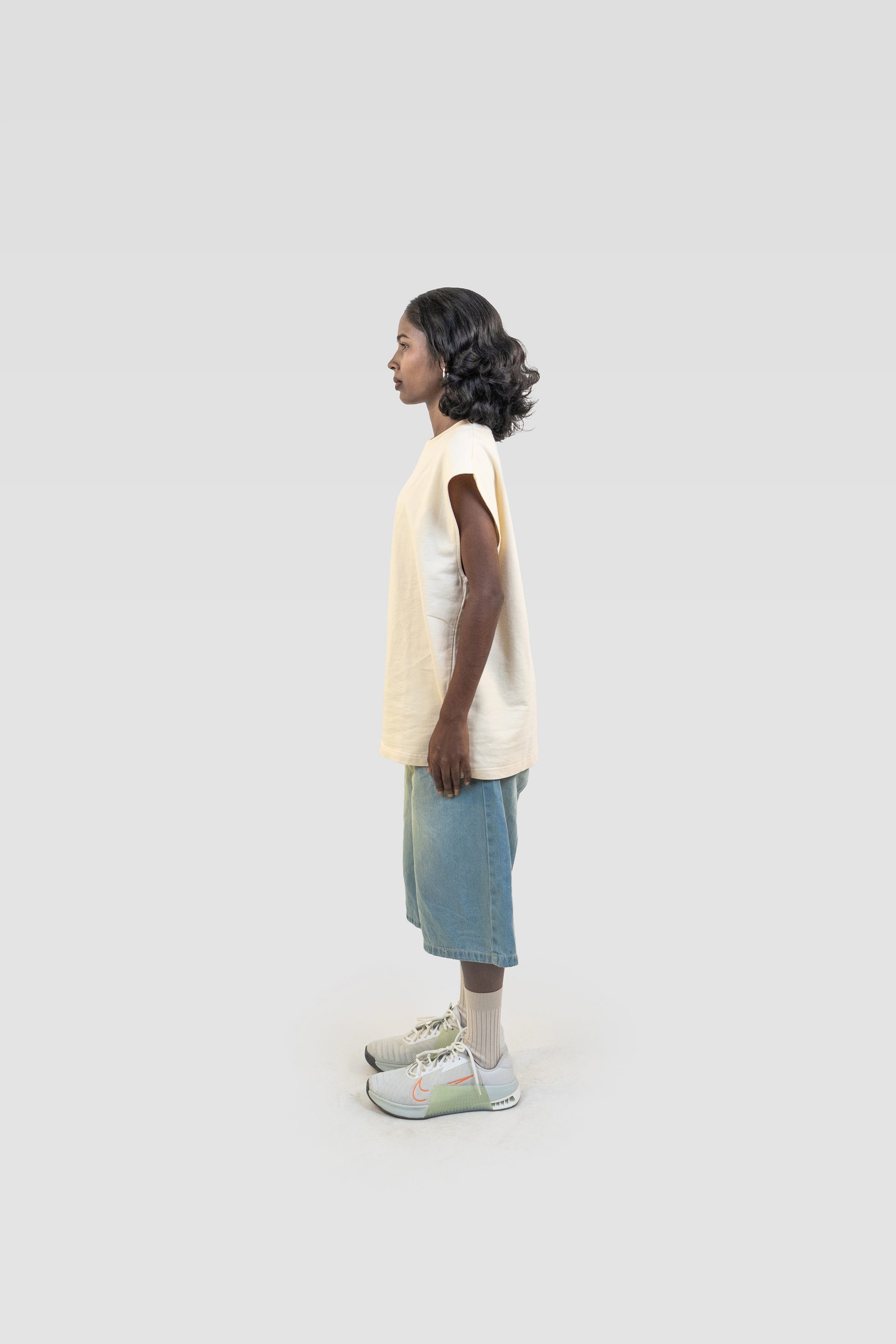 Full-body side profile of model wearing the Harper Slein Foundation Tank in OG Off White, styled with denim shorts and sneakers against a plain background.
