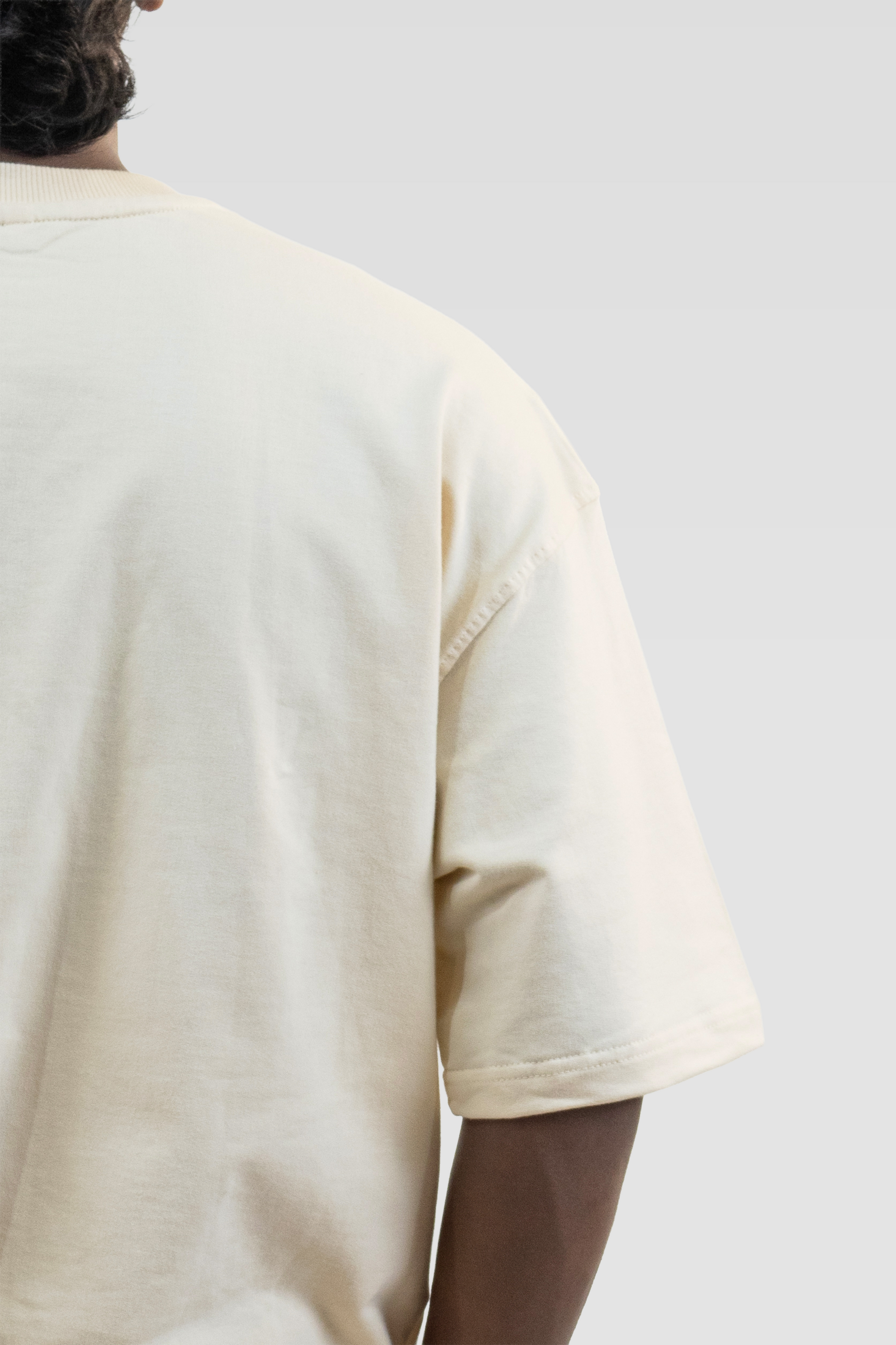Back close-up of a model wearing Harper Slein Off White oversized tee in premium 240 GSM cotton, focusing on the smooth fabric, precise stitching, and relaxed sleeve drape against a plain background.