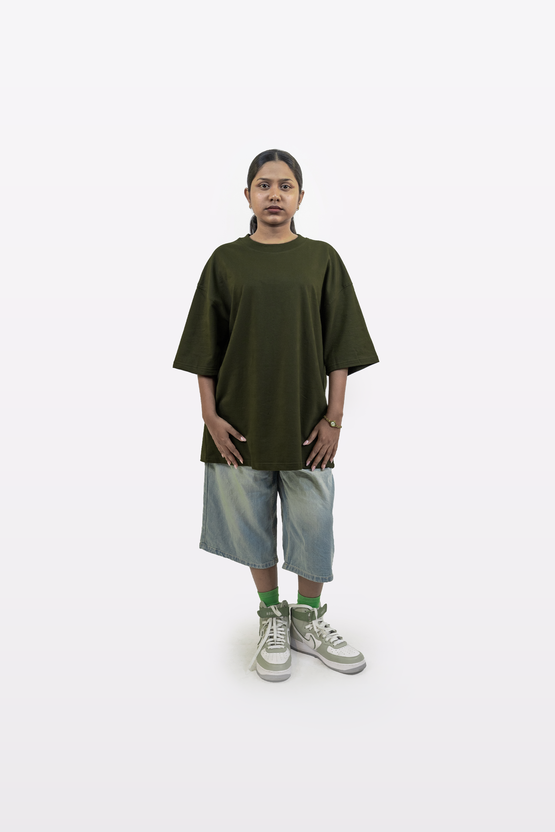 Full-body shot of a female model wearing the Harper Slein oversized t-shirt in Nori Seaweed Green, paired with knee-length denim shorts and green-accent sneakers, on a white background.