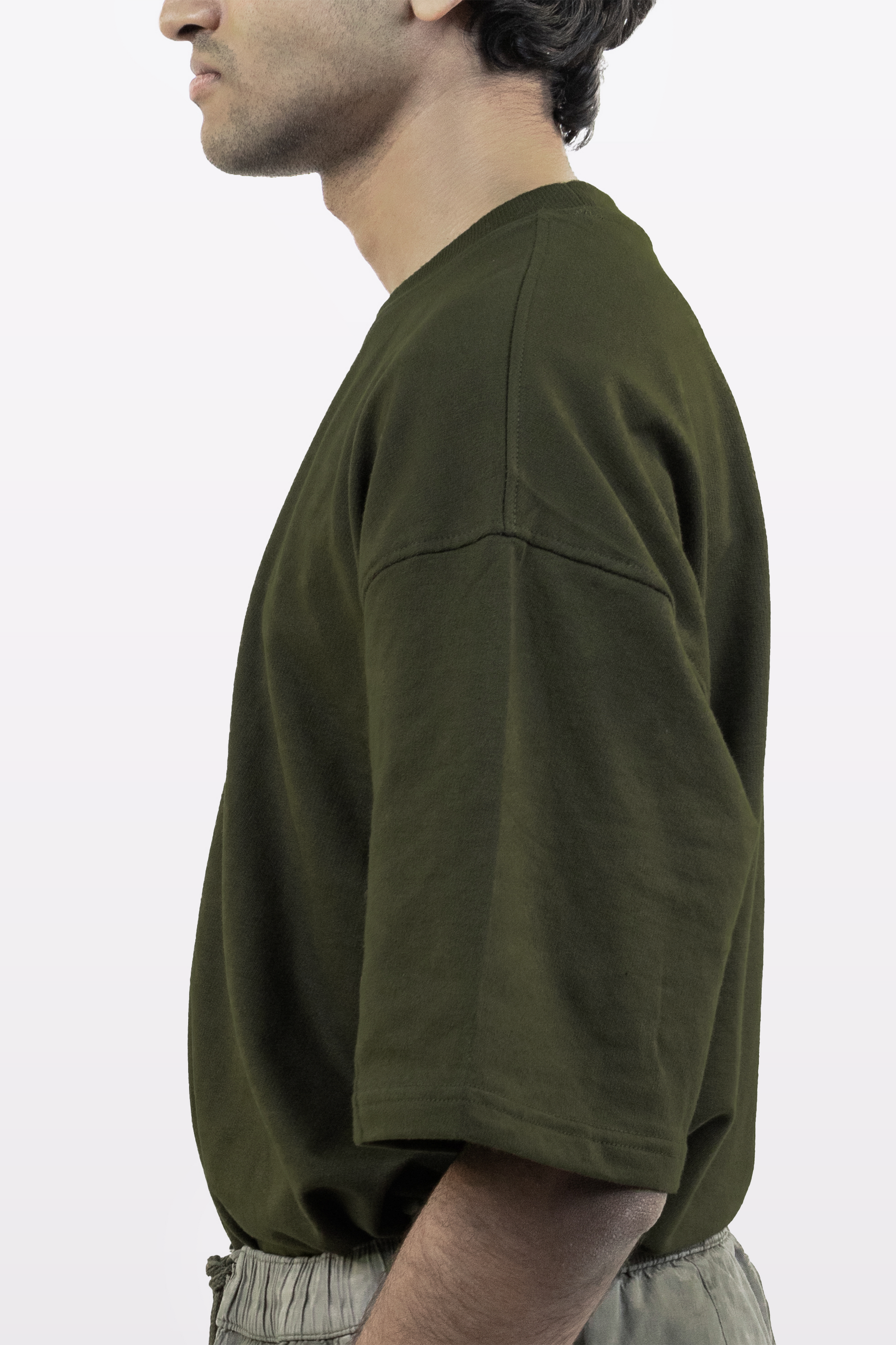 Side profile of a male model wearing the Harper Slein oversized t-shirt in Nori Seaweed Green, paired with light gray drawstring pants, against a white background.