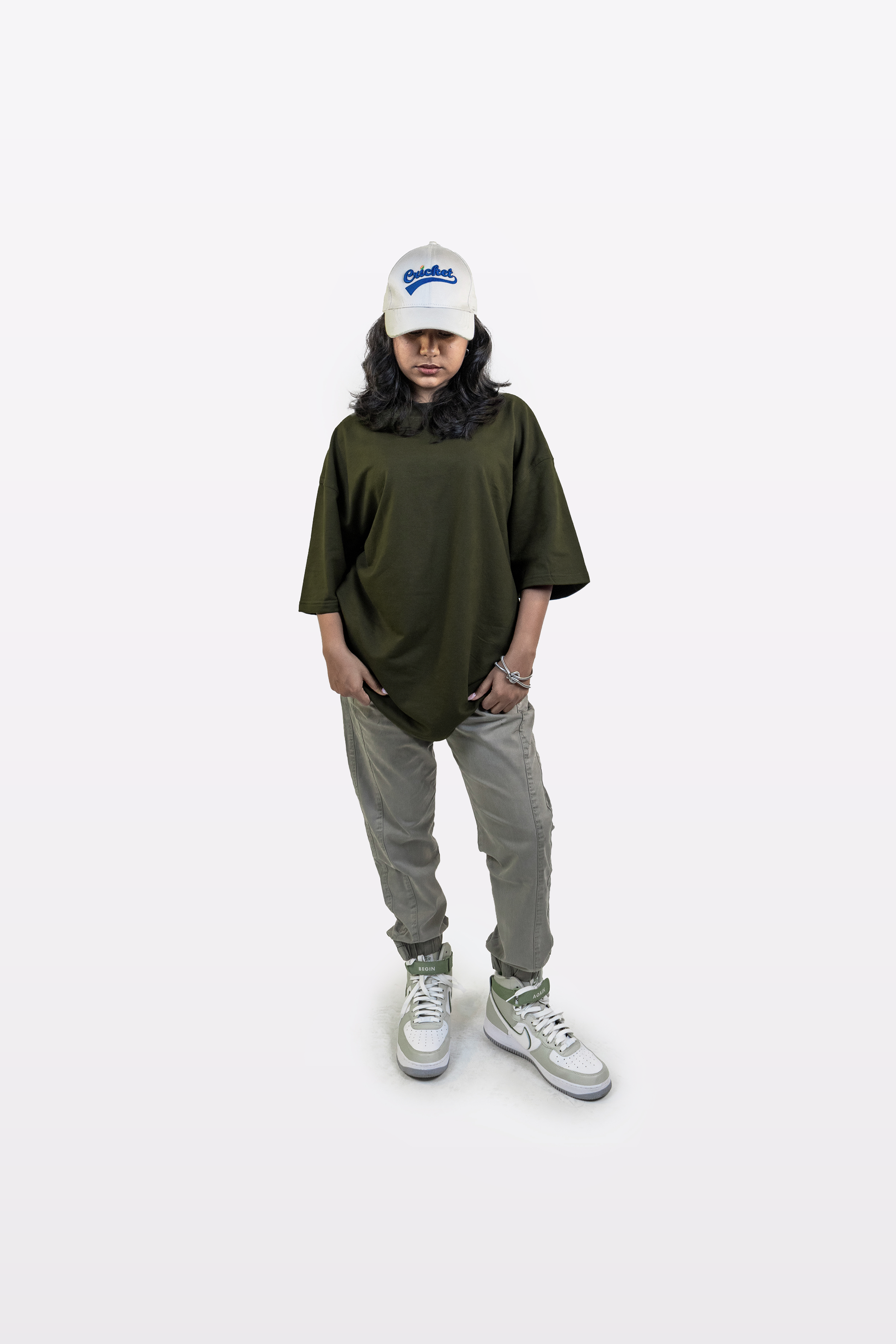 Full-body view of a model wearing the Harper Slein oversized t-shirt in Nori Seaweed Green, paired with gray pants and a white cap, standing against a white background.