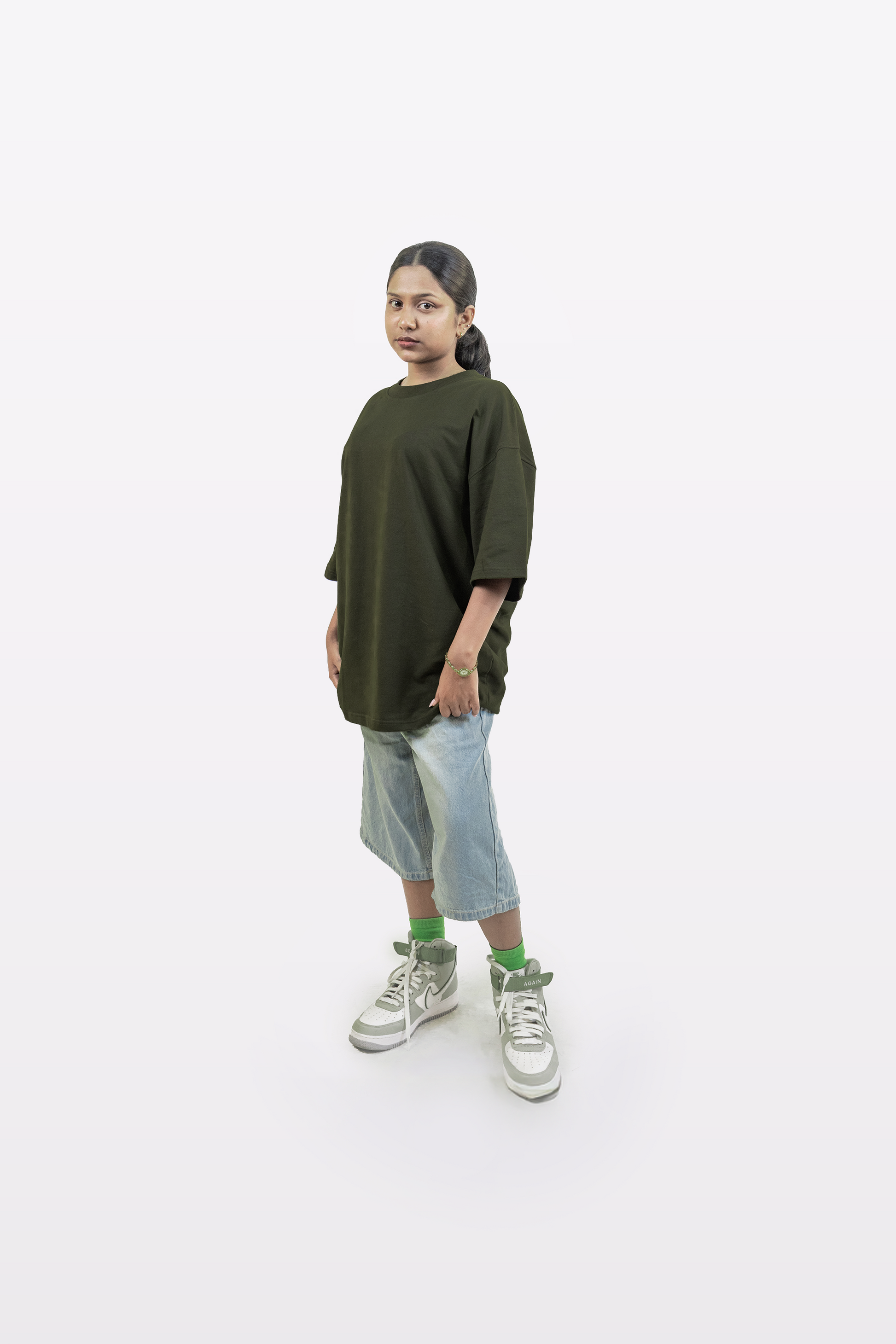 Full-body view of a model wearing the Harper Slein oversized t-shirt in Nori Seaweed Green, paired with light blue denim shorts and green socks, standing against a white background.