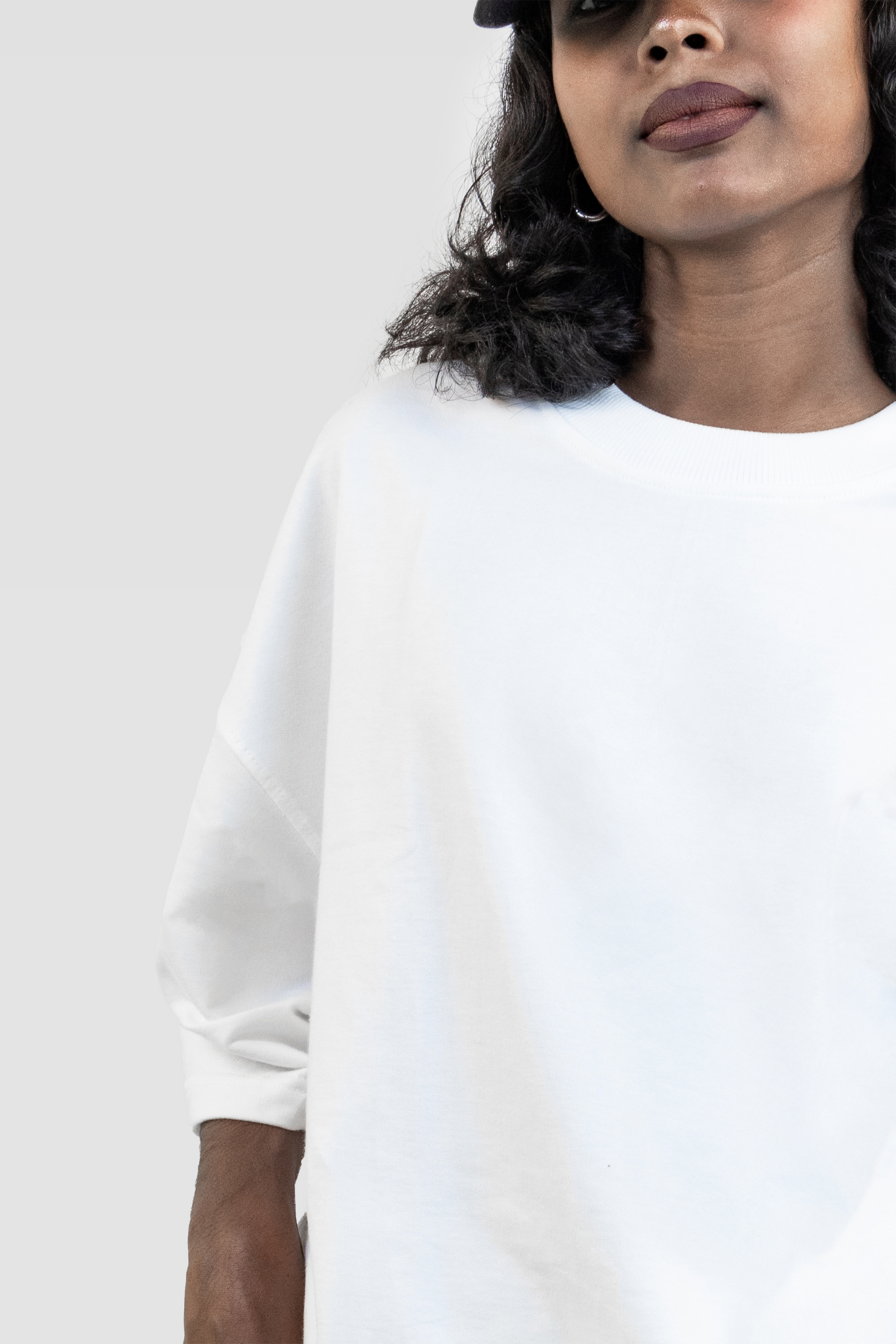Front close-up of a female model wearing Harper Slein oversized t-shirt in Blank White, highlighting neckline and sleeve details against a light gray background