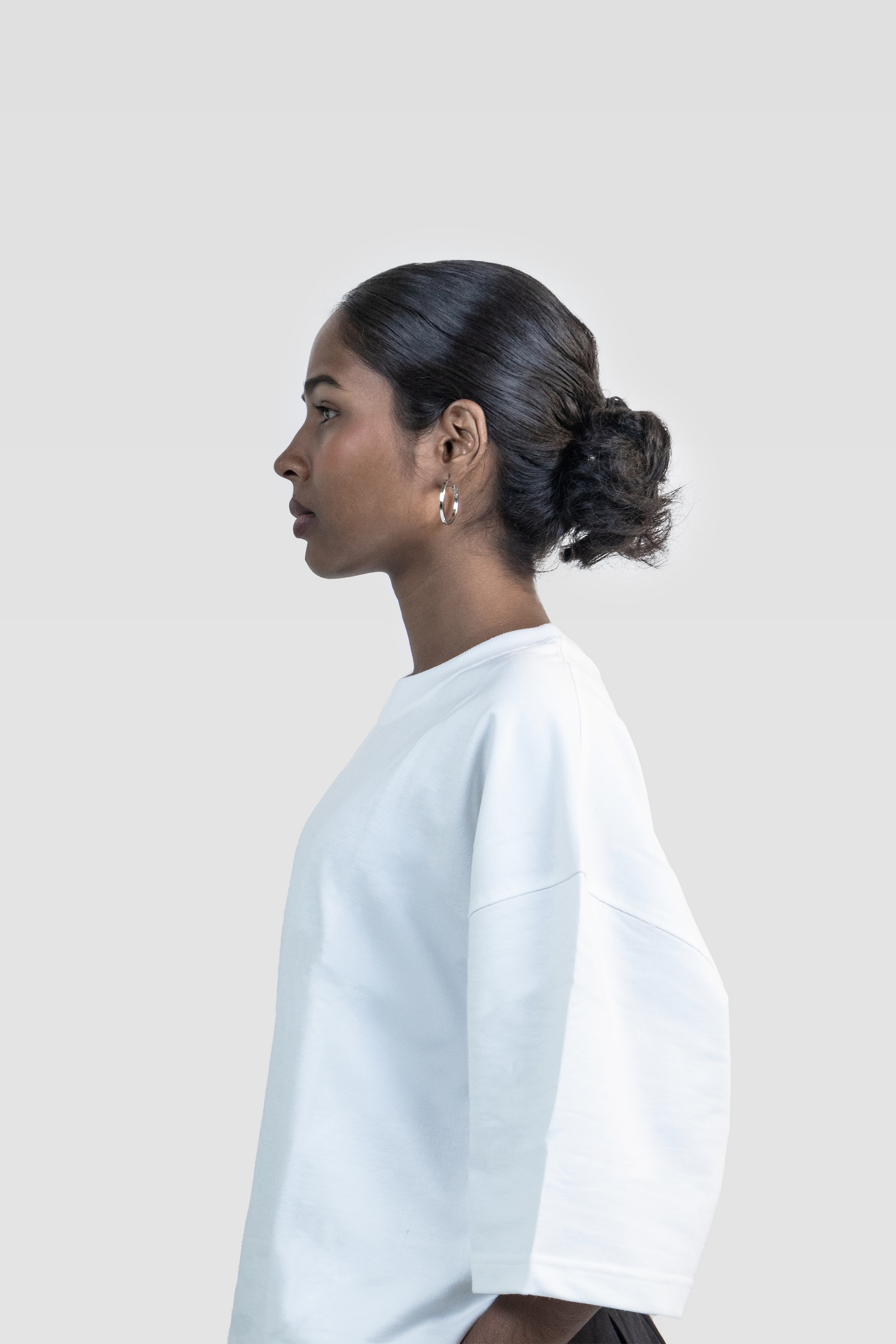 Side profile close-up of a female model wearing Harper Slein oversized t-shirt in Blank White against a light gray background