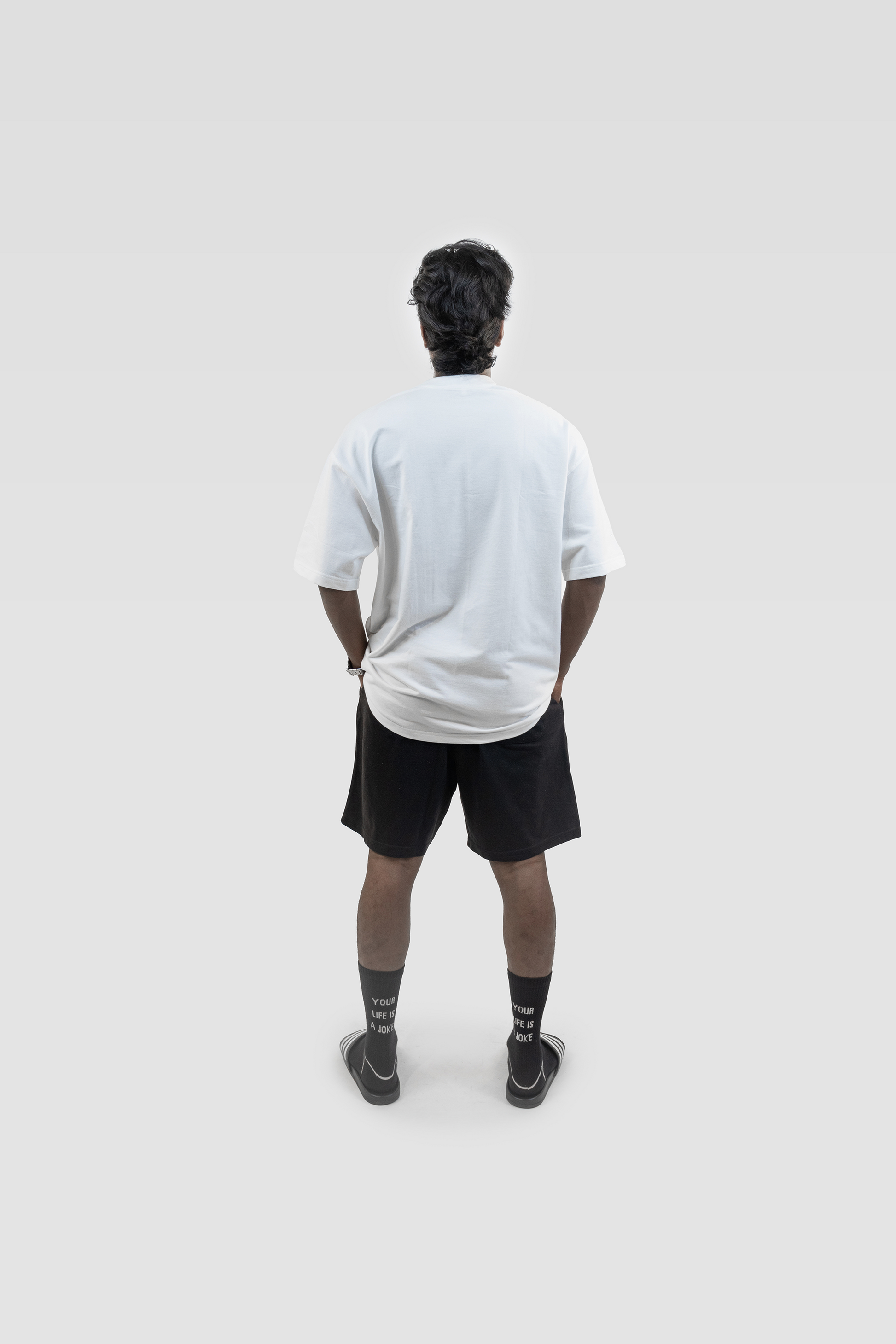 Full back view of a model wearing Harper Slein oversized t-shirt in Blank White, styled with black shorts, against a light gray background