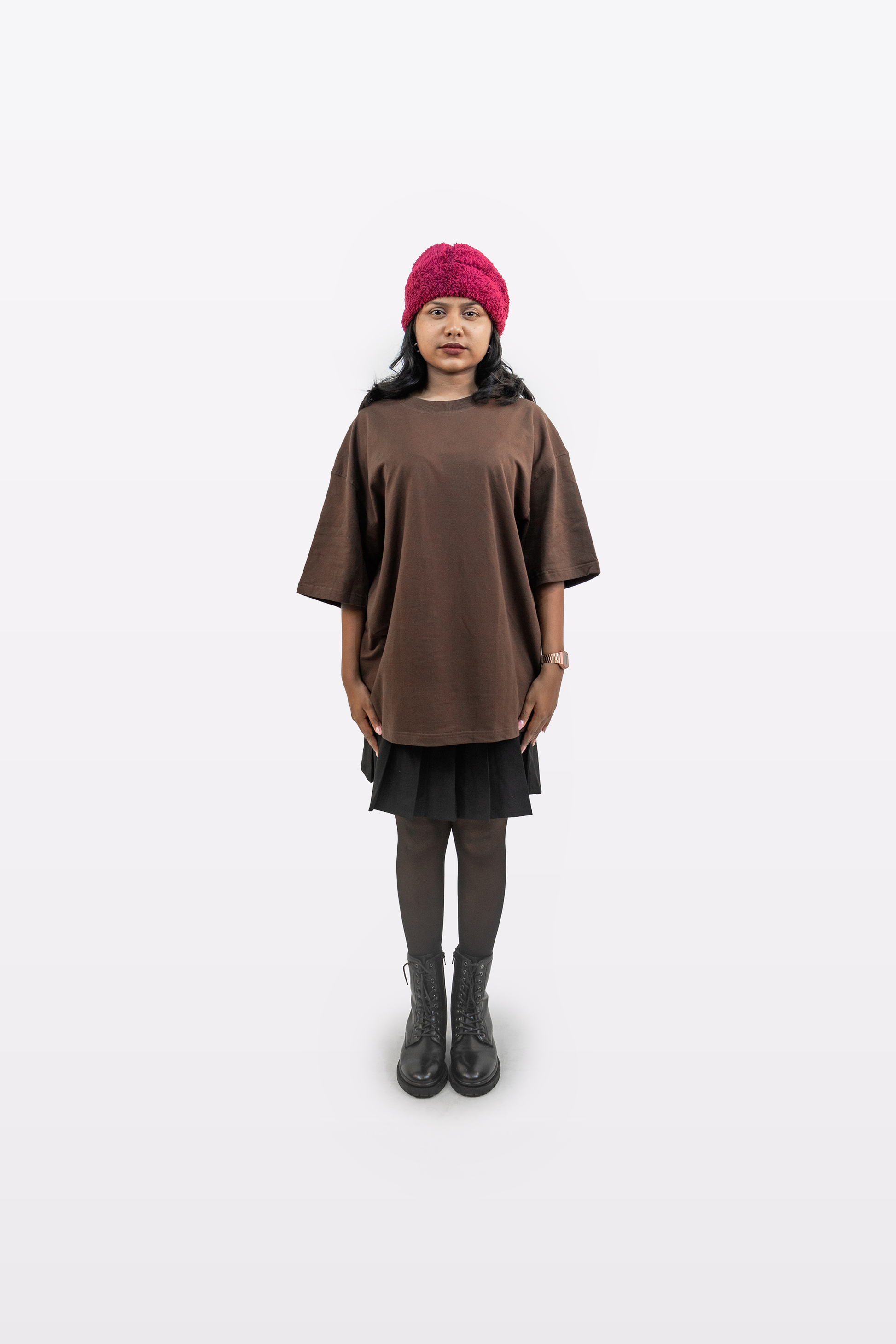 Front view of a female model wearing Harper Slein oversized t-shirt in Cacao paired with a black skirt, tights, black boots, and a red beanie on a white background