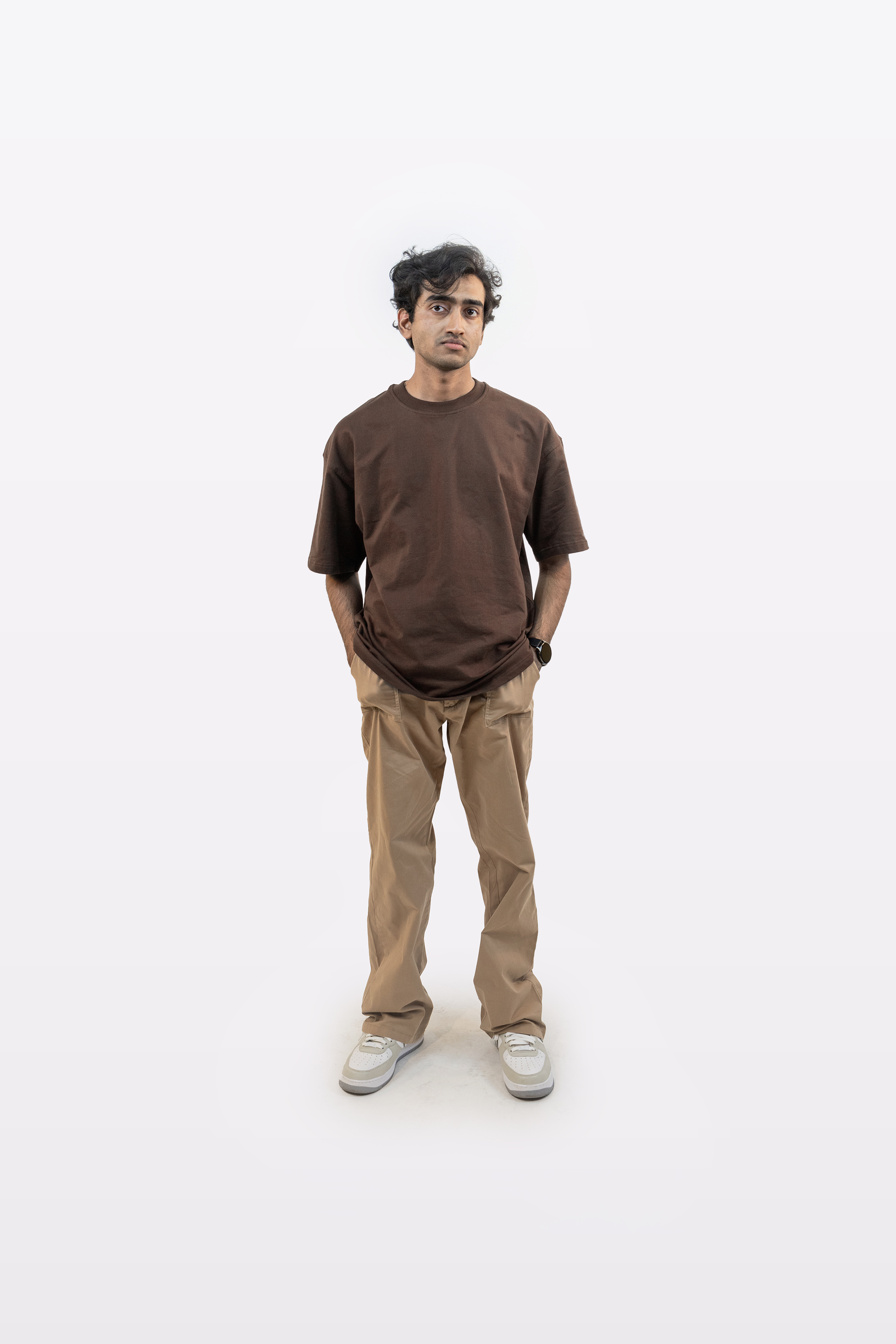 Full body front view of a model wearing Harper Slein oversized t-shirt in Cacao with beige pants and hands in pocket on a white background