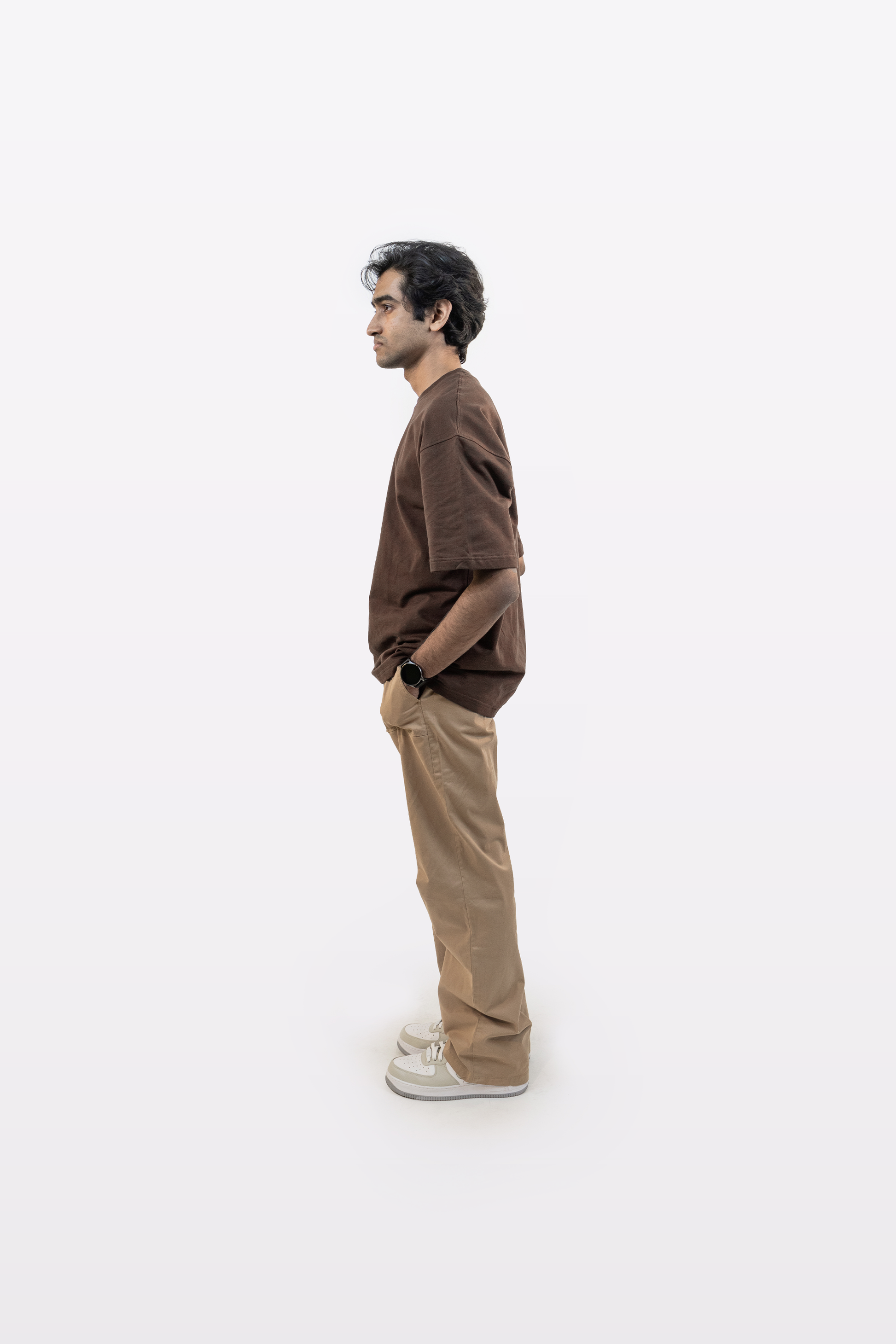 Full body side profile of a model wearing Harper Slein oversized t-shirt in Cacao with beige pants and hands in pocket on a white background