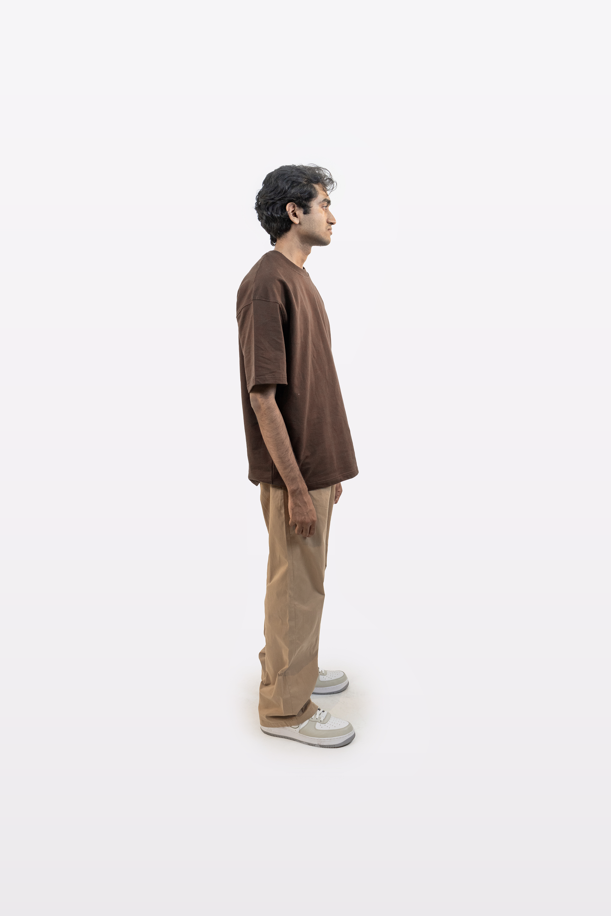 Full body side profile of a model wearing Harper Slein oversized t-shirt in Cacao with beige pants on a white background