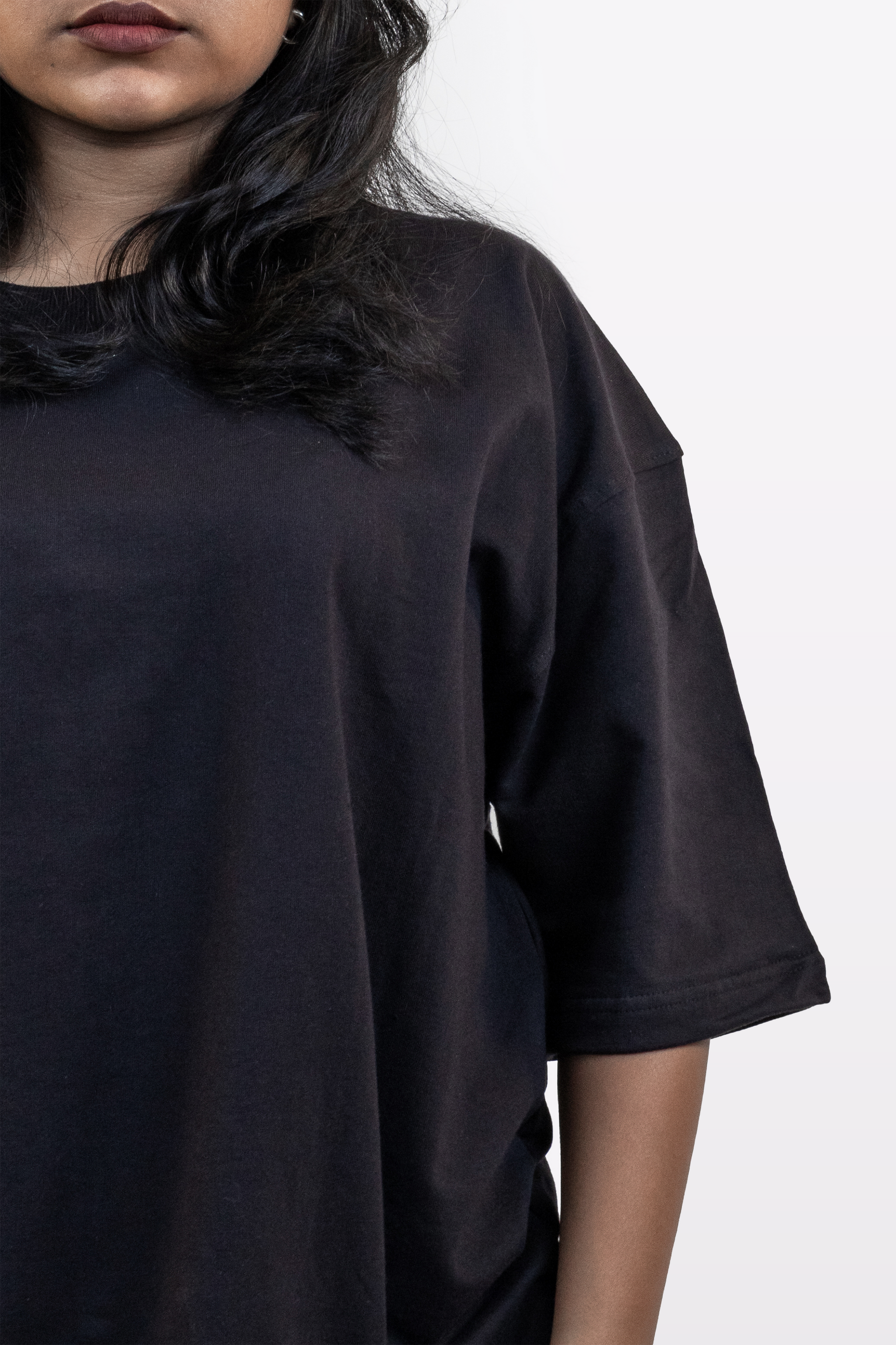 Close-up of female model wearing Harper Slein oversized t-shirt in Classic Black, focusing on neckline, sleeve, and fabric drape against a white background