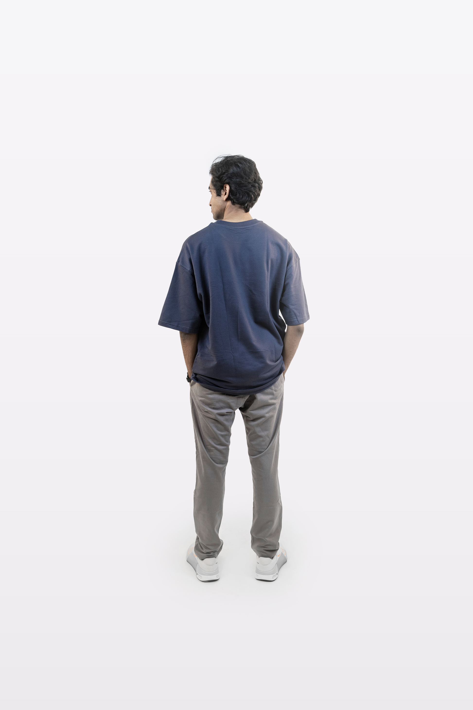 Model wearing Harper Slein oversized t-shirt in Compass Blue with gray pants, back view, on a white background