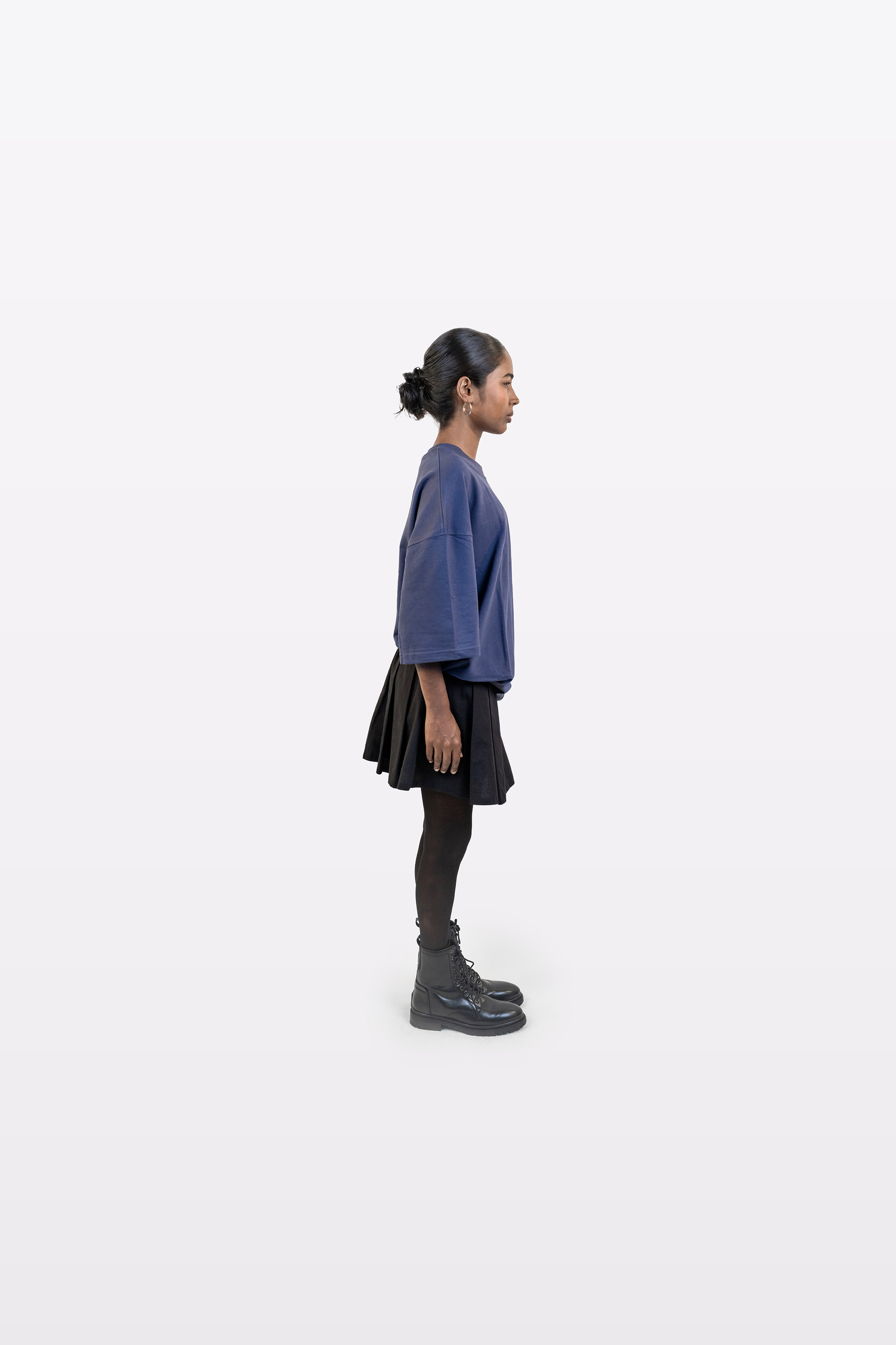 Model wearing Harper Slein oversized t-shirt in Compass Blue styled with a black skirt and boots, side profile view, on a white background