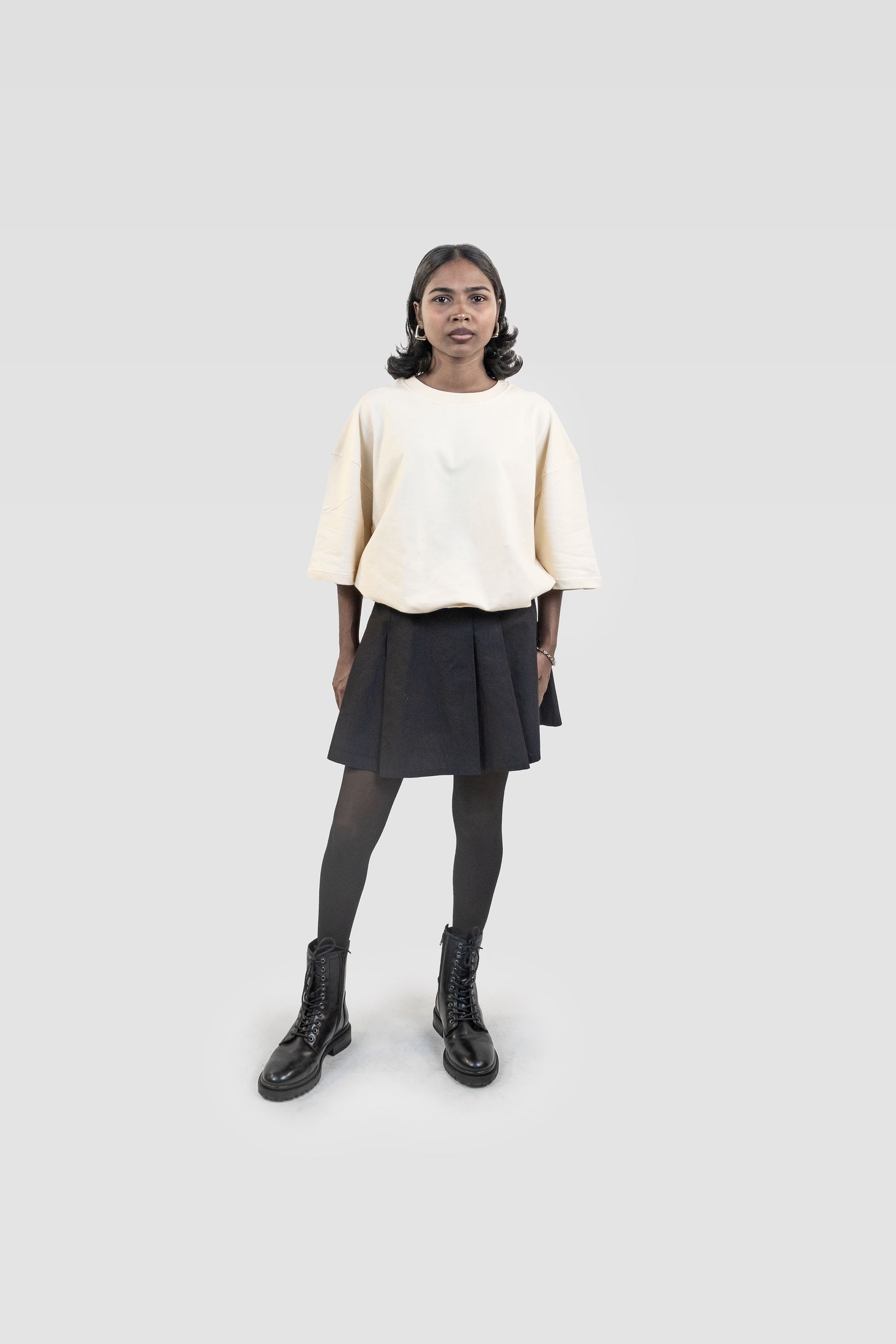 Front view of model wearing Harper Slein oversized t-shirt in OG Off White styled with black skirt, tights, and boots on a white background