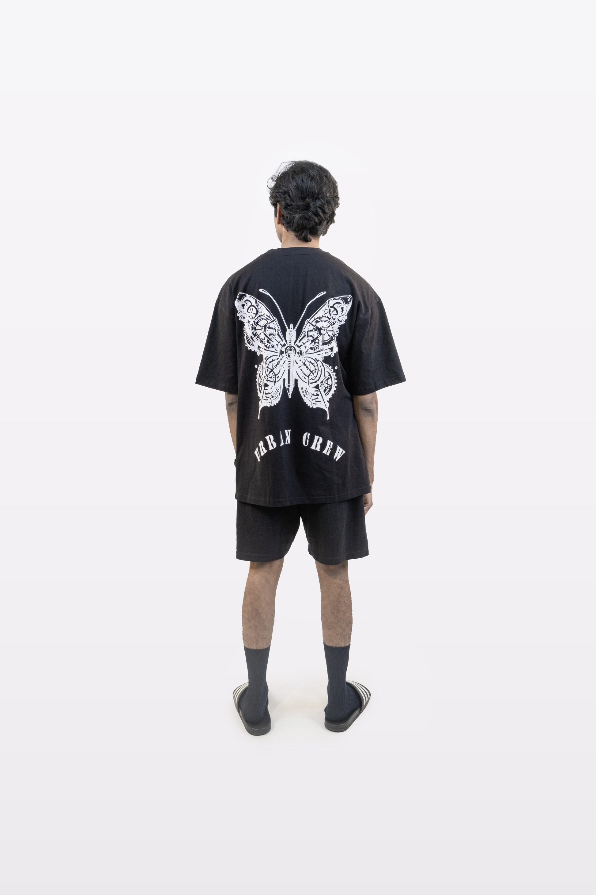 Model wearing the Harper Slein Urban Crew Collection T-Shirt in black, featuring a large white mechanical butterfly graphic and ‘Urban Crew’ text on the back, photographed against a white background.