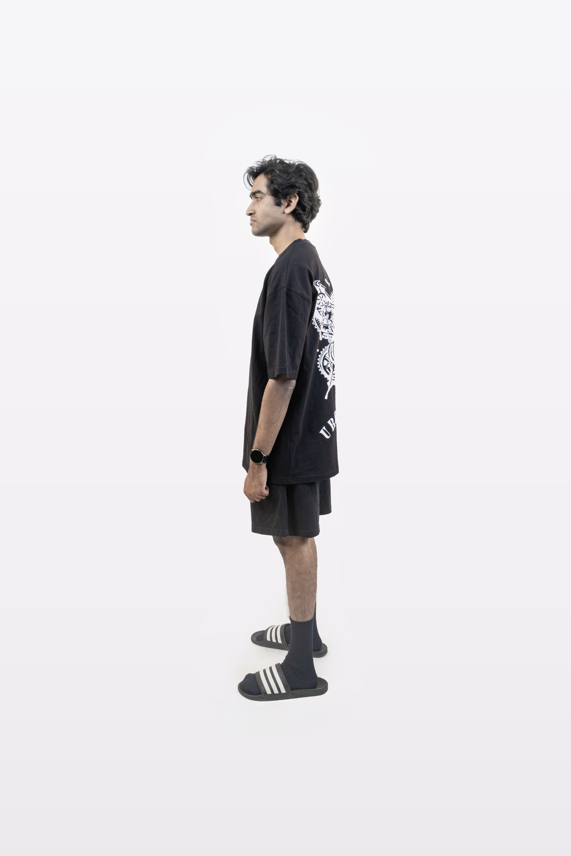 Model in side profile wearing the Harper Slein Urban Crew Collection T-Shirt in black, featuring a large white butterfly graphic and ‘Urban Crew’ text on the back, paired with black shorts and sandals, against a white background.