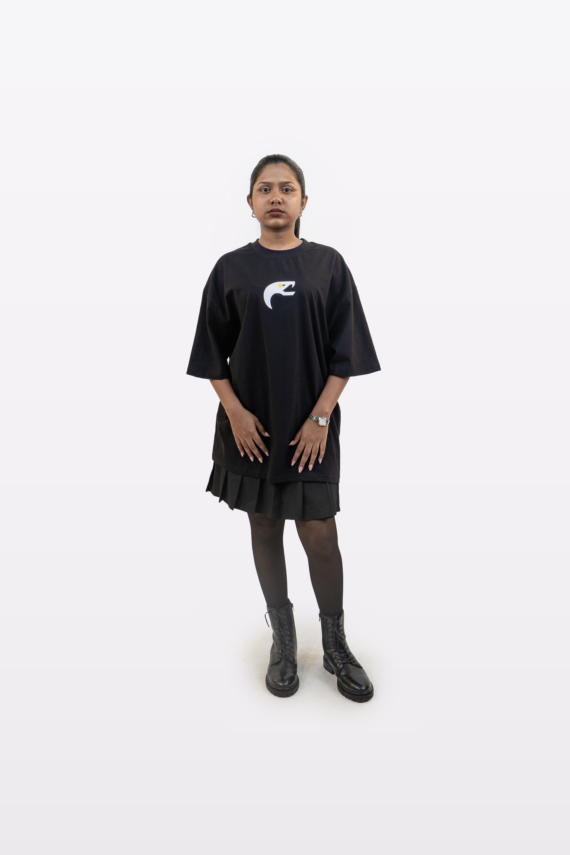 Model wearing the Harper Slein Urban Crew Collection T-Shirt in black, featuring a minimalist white snake emblem on the chest, paired with a black pleated skirt, tights, and boots, standing against a white background.