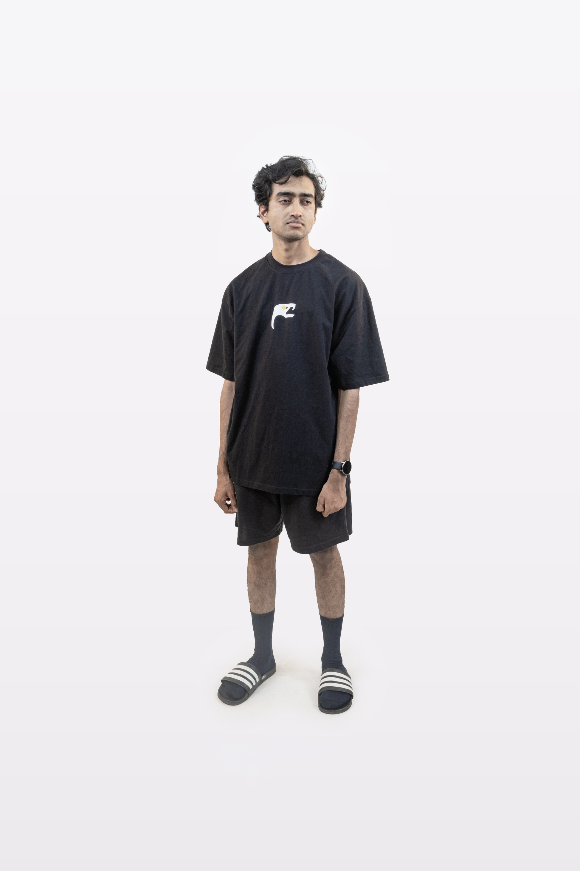 Model wearing the Harper Slein Urban Crew Collection T-Shirt in black, featuring a small white snake emblem on the chest, paired with black shorts and sandals, standing against a white background.