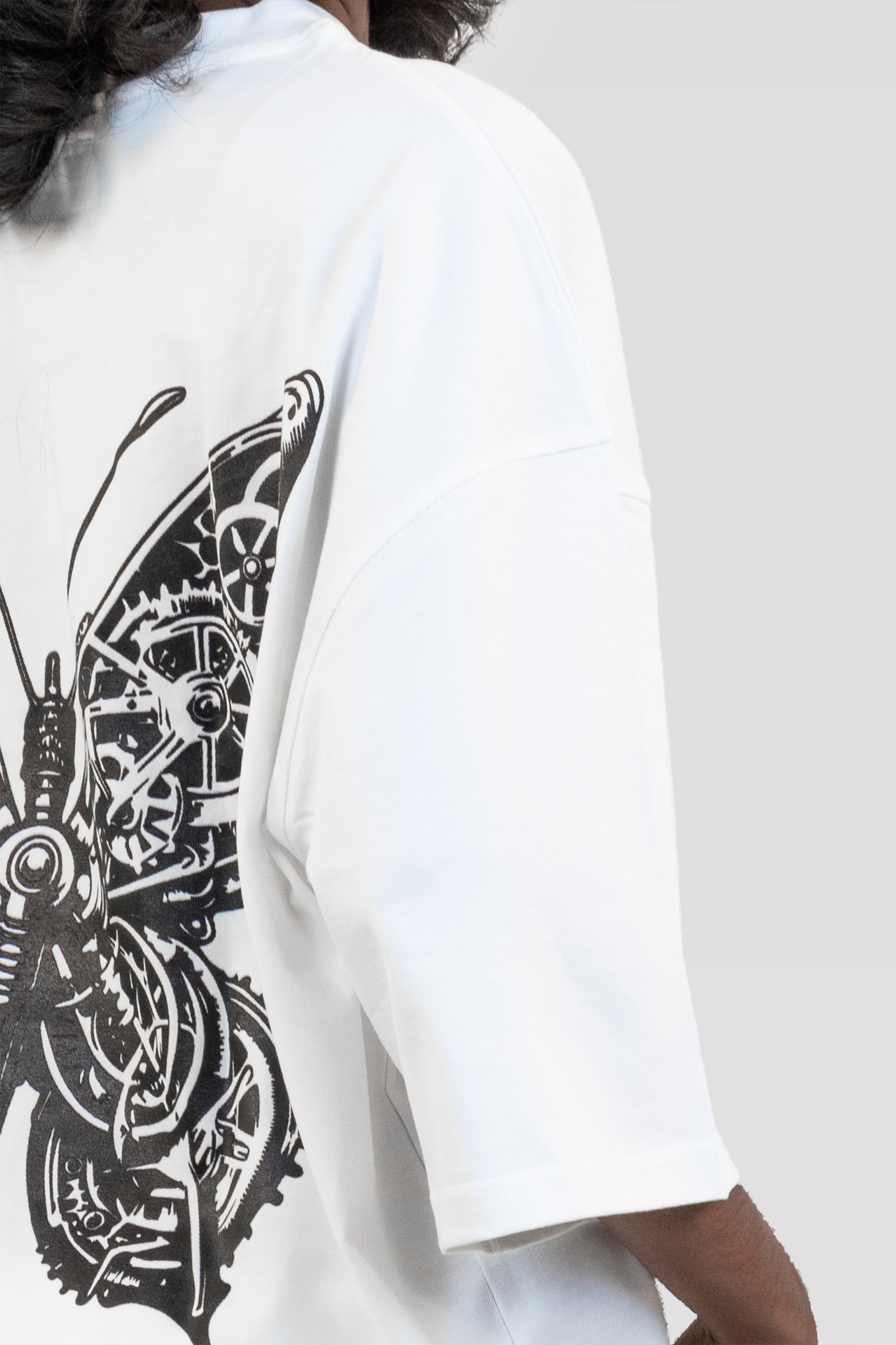 Close-up side view of the Harper Slein Urban Crew Collection Butterfly T-Shirt in white, showcasing the black mechanical butterfly artwork on the back, worn by a model against a light grey background.