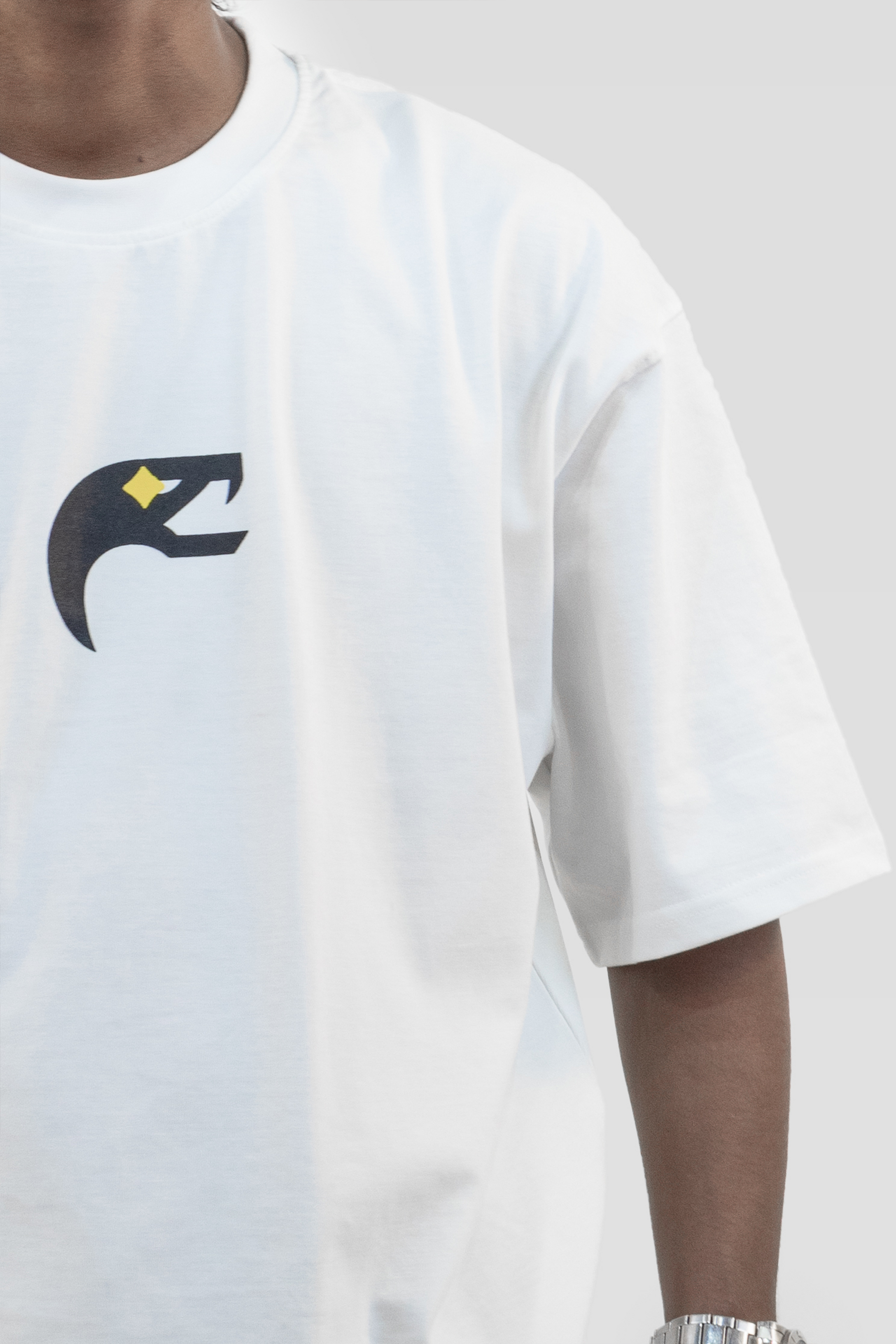 Close-up front view of the Harper Slein Urban Crew Collection Butterfly T-Shirt in white, featuring a black and yellow serpent logo, worn by a model against a light grey background.