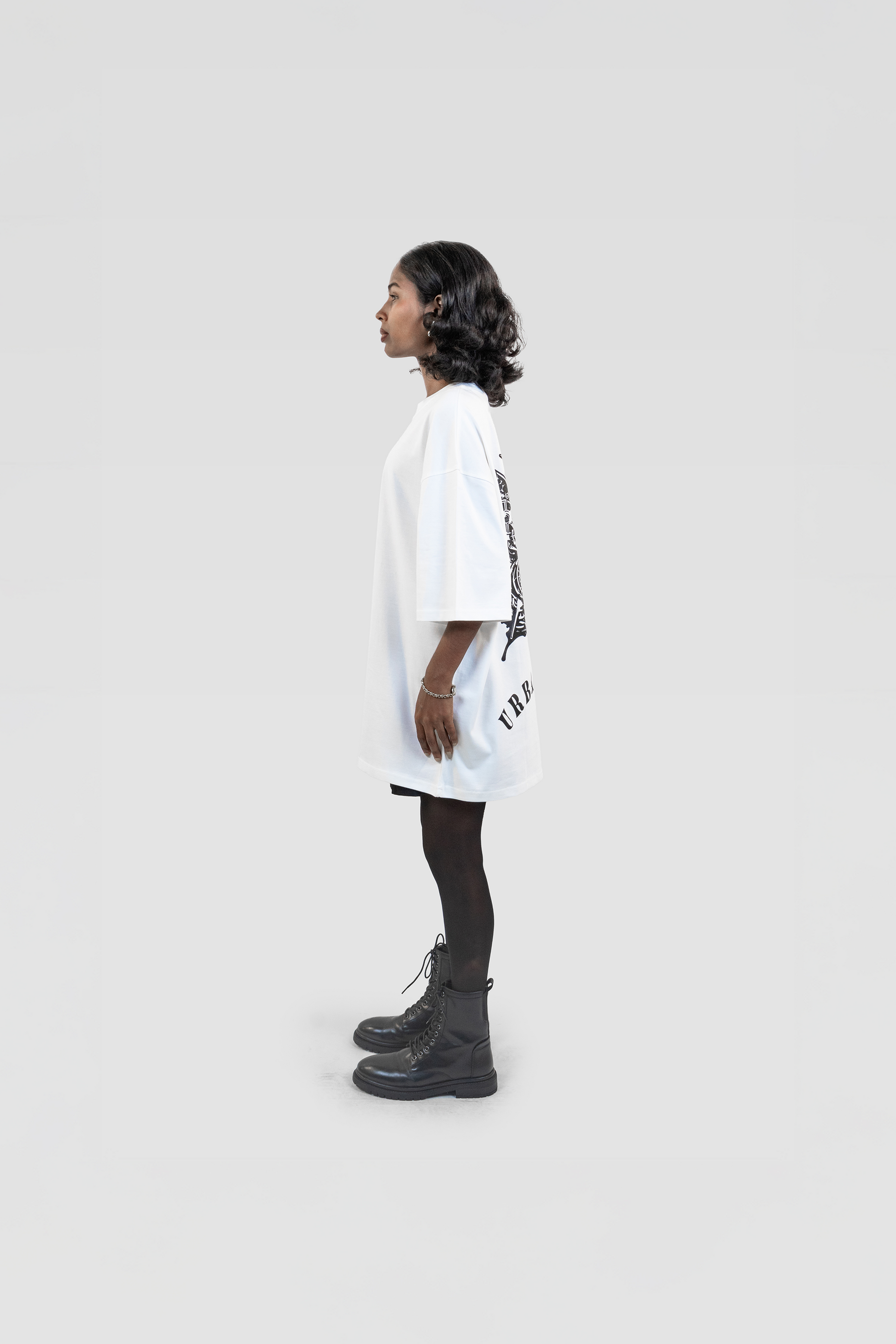 Side profile view of the Harper Slein Urban Crew Collection Butterfly T-Shirt in white, featuring a large black butterfly graphic on the back, worn by a model with black skirt and combat boots against a light grey background.