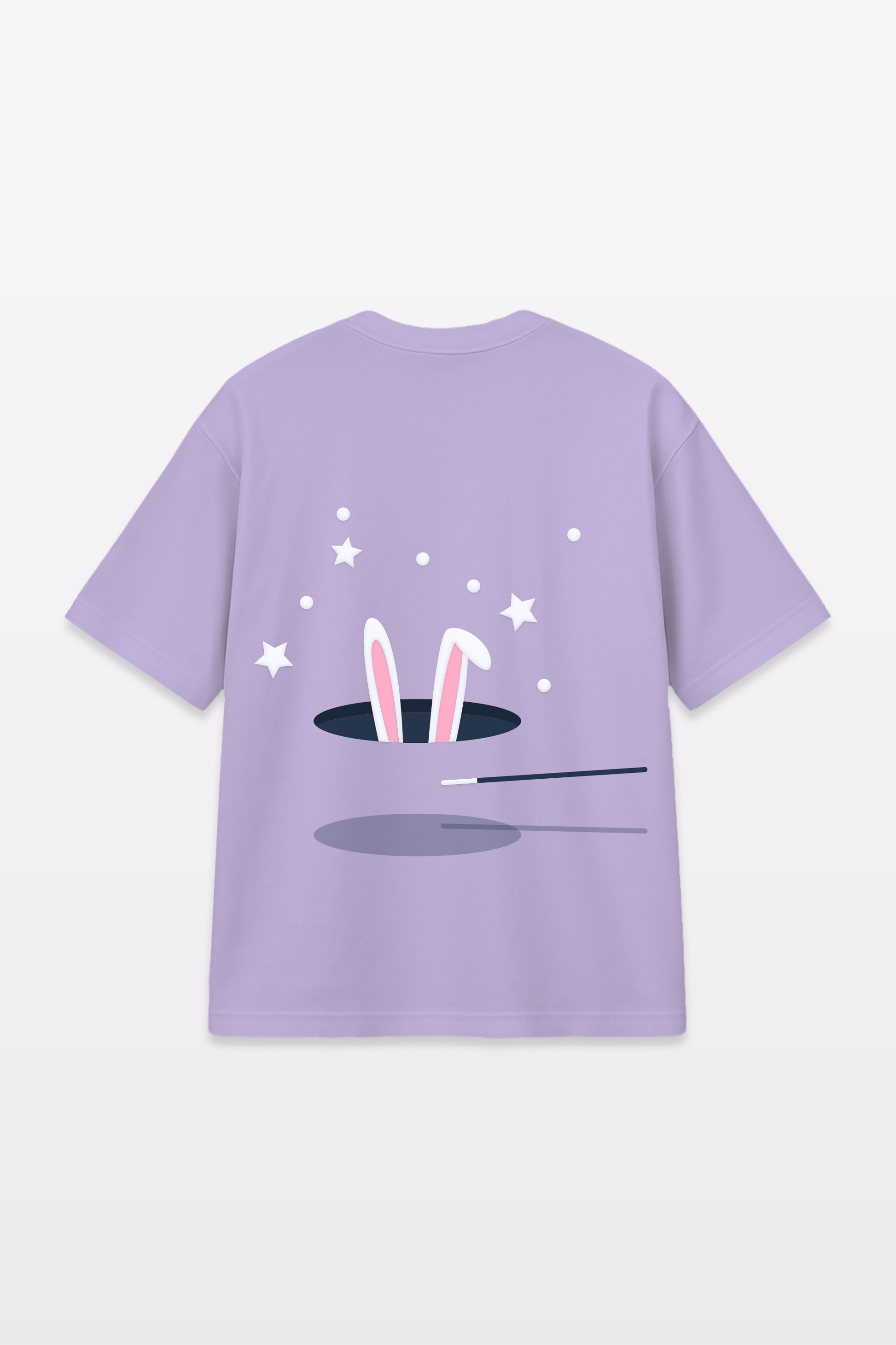Flat lay of a lavender t-shirt with a graphic of bunny ears emerging from a magician’s hat, surrounded by stars and a magic wand, displayed on a plain white background.
