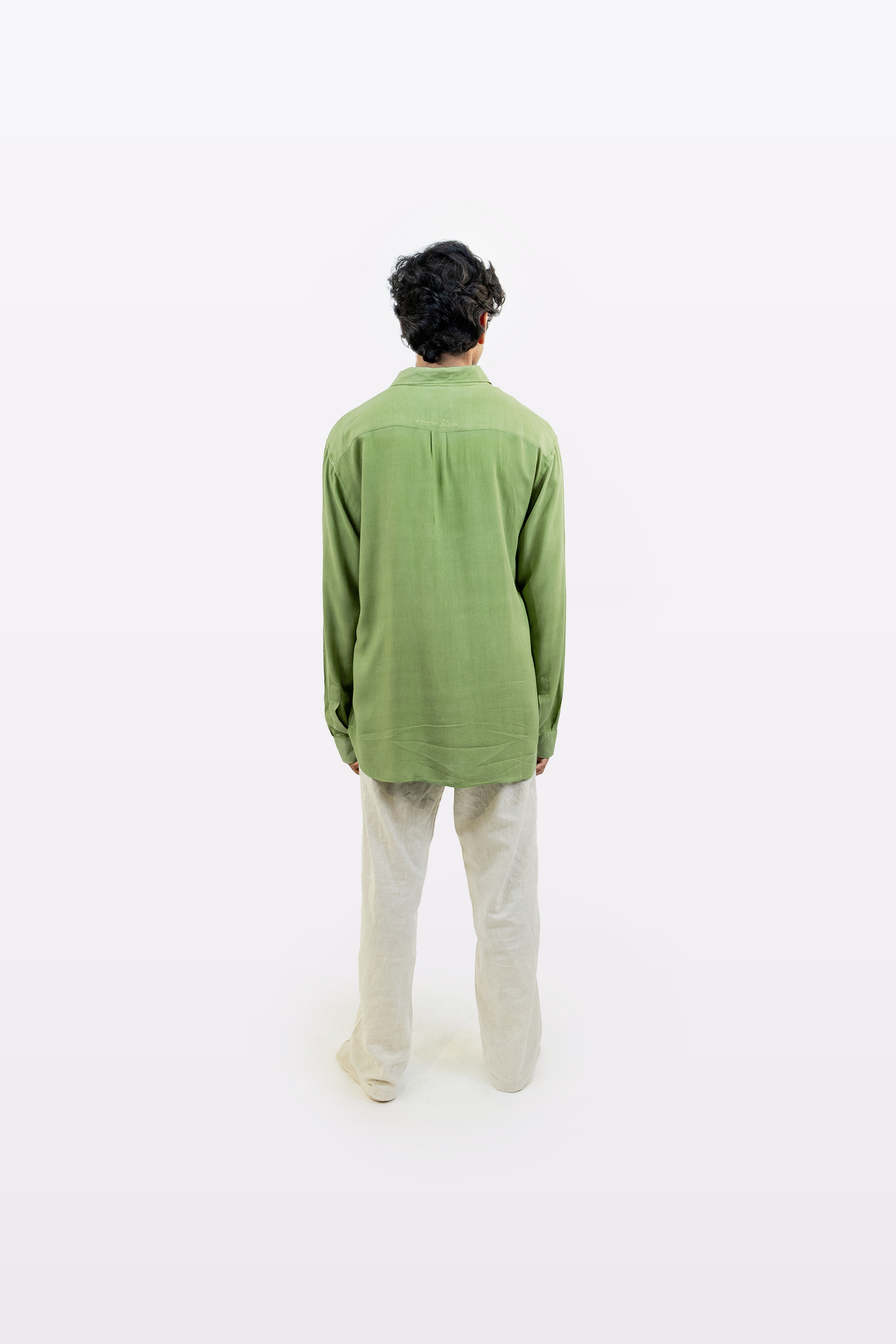 Full-body back view of a model wearing the Harper Slein Moss Shirt in green, paired with beige pants, against a white background