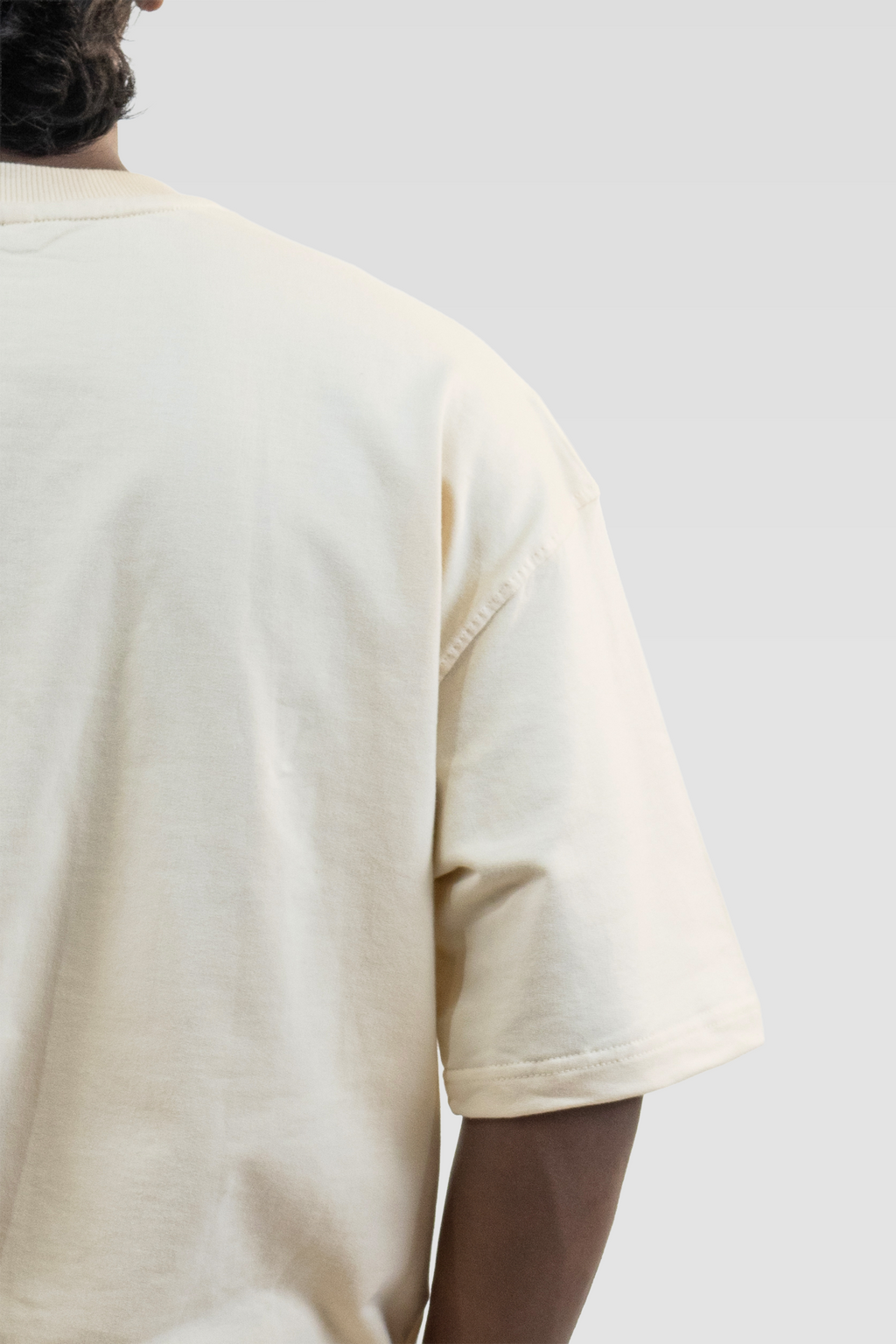 Back close-up of a model wearing Harper Slein Off White oversized tee in premium 240 GSM cotton, focusing on the smooth fabric, precise stitching, and relaxed sleeve drape against a plain background.