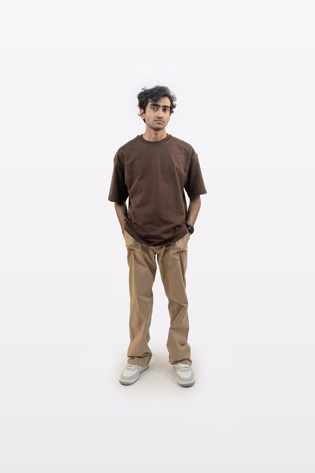 Full body front view of a model wearing Harper Slein oversized t-shirt in Cacao with beige pants and hands in pocket on a white background