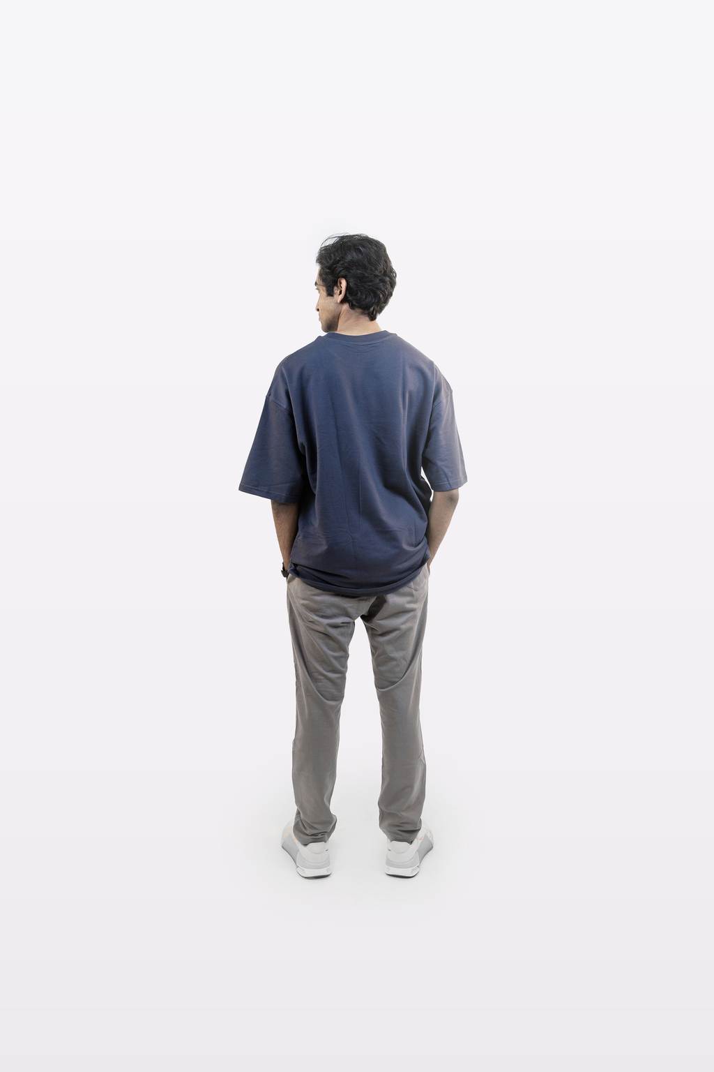 Model wearing Harper Slein oversized t-shirt in Compass Blue with gray pants, back view, on a white background