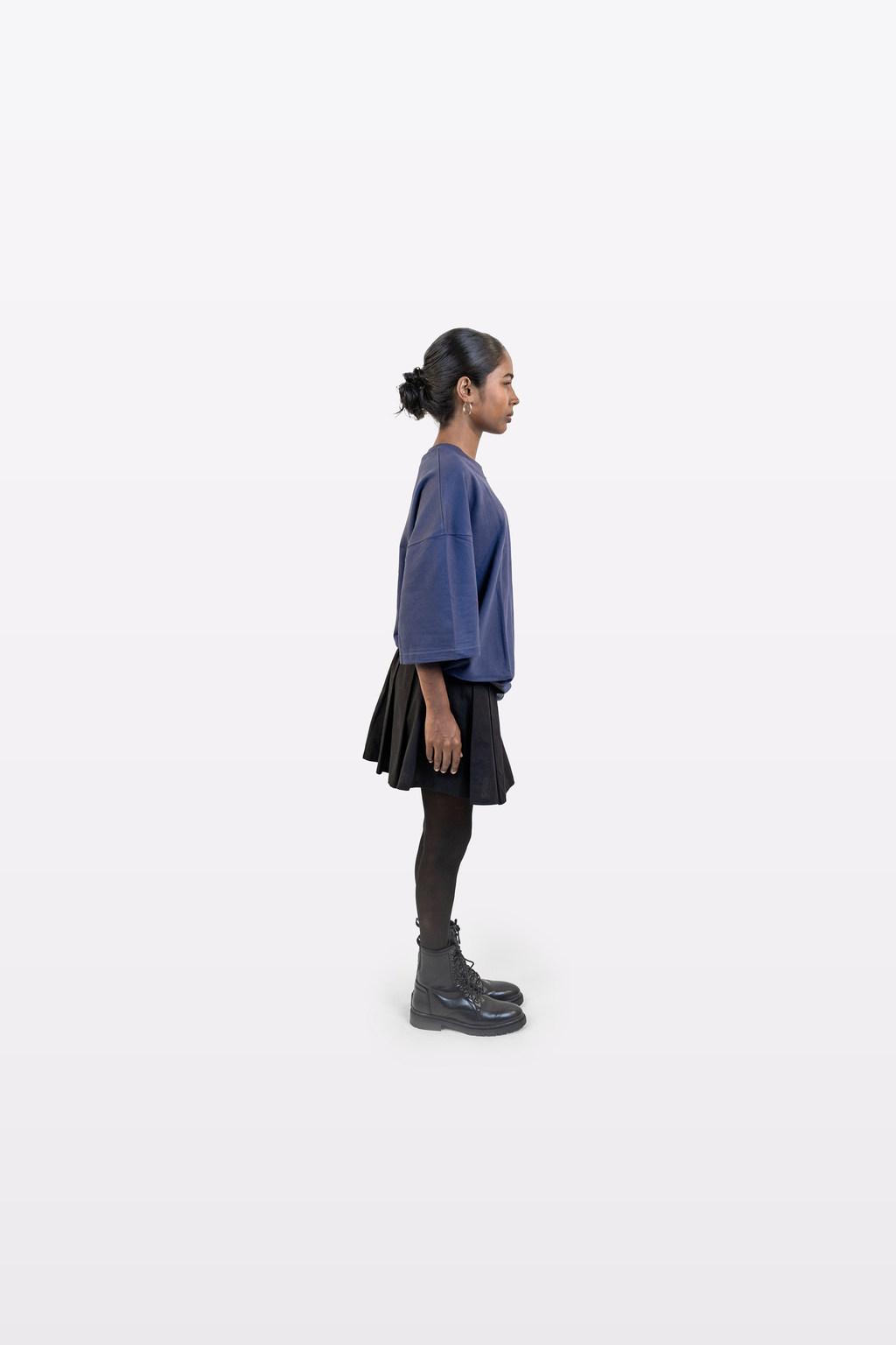 Model wearing Harper Slein oversized t-shirt in Compass Blue styled with a black skirt and boots, side profile view, on a white background