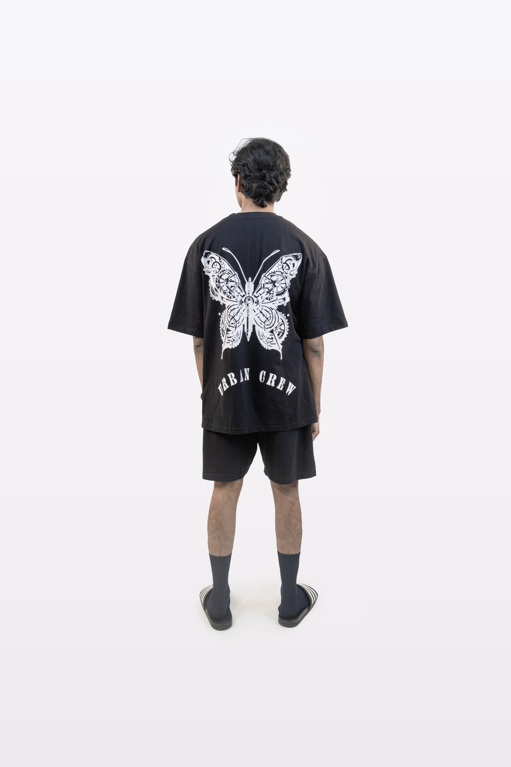 Model wearing the Harper Slein Urban Crew Collection T-Shirt in black, featuring a large white mechanical butterfly graphic and ‘Urban Crew’ text on the back, photographed against a white background.